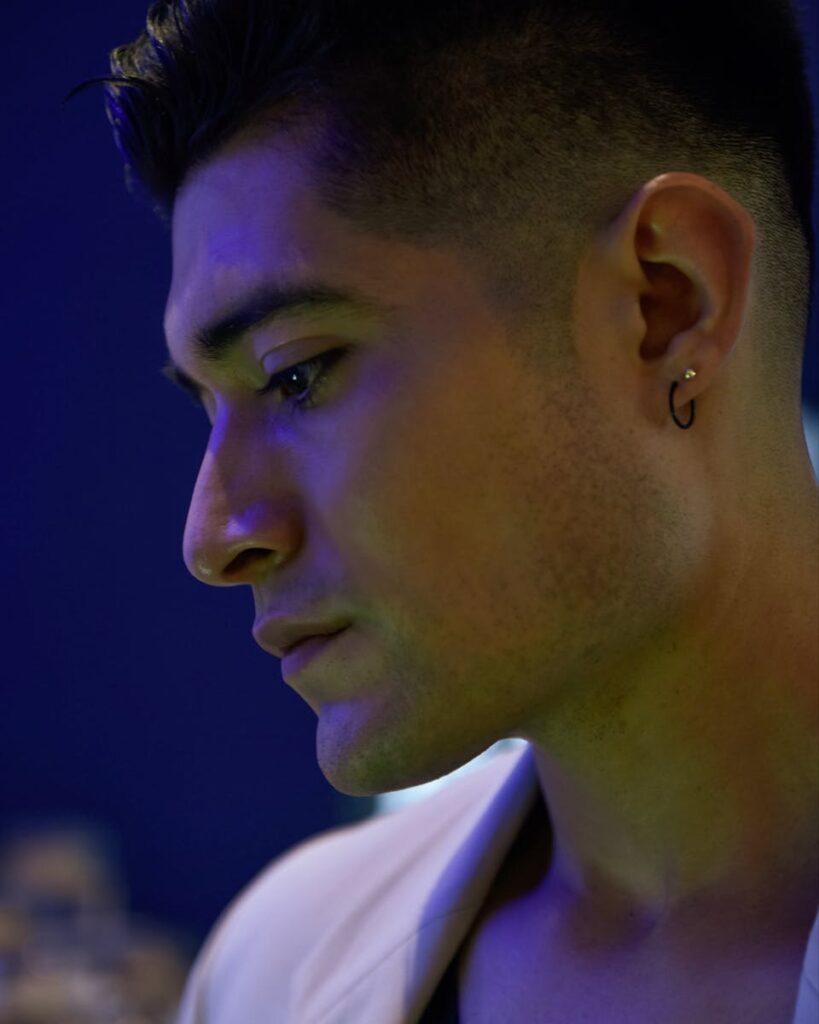 Close-up portrait of a young Hispanic man with ear piercing and stylish haircut at night.