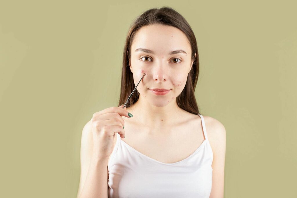 Woman using a blackhead extractor on her face against a light green background.
