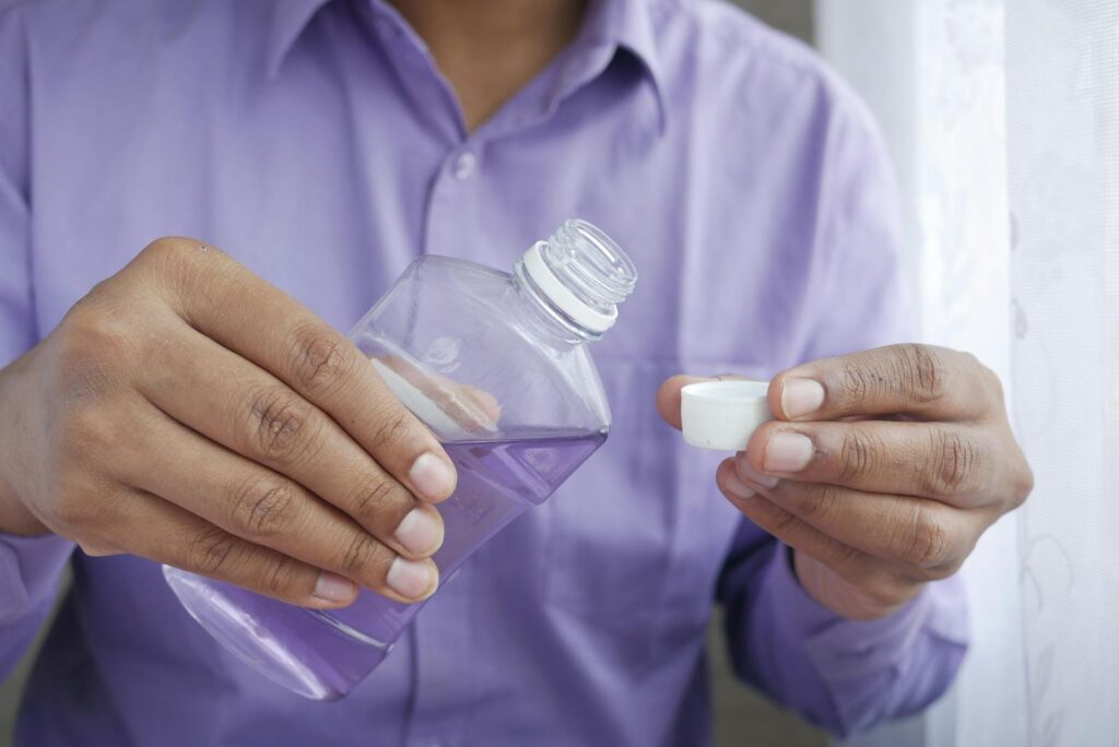 Close-up of hands holding a purple plastic bottle while pouring mouthwash into a cap.