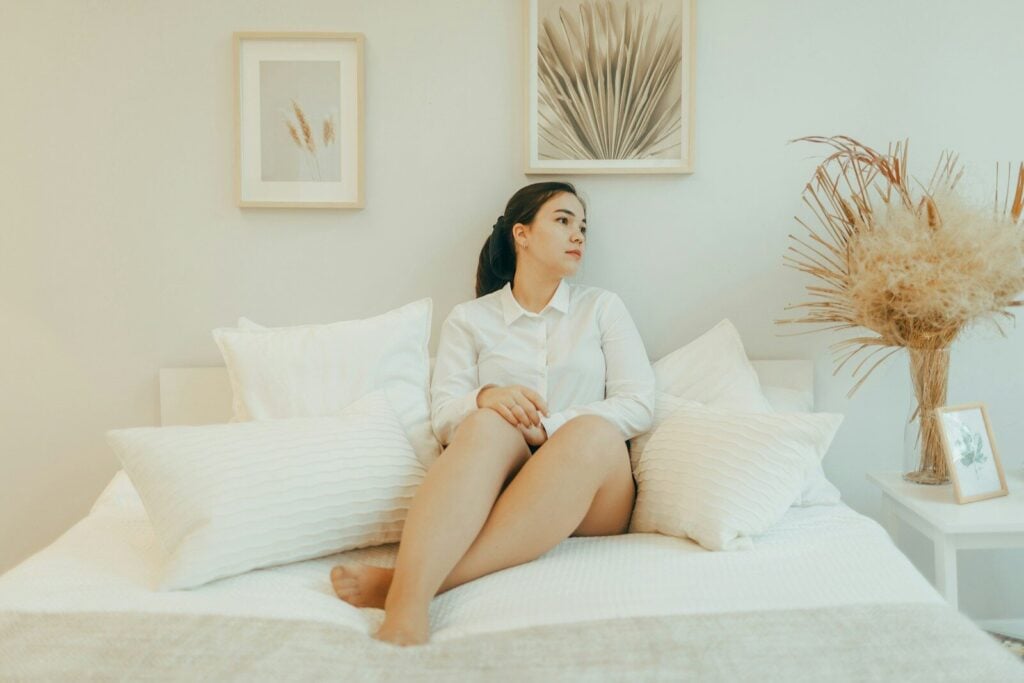 Woman in white shirt sitting on a bed.