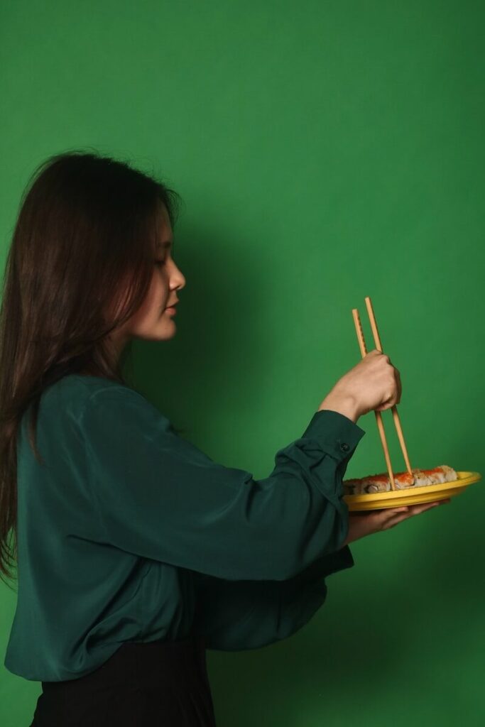 a woman holding a plate of food with chopsticks