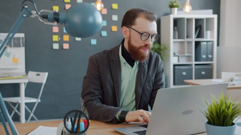 Bearded man working on a laptop in an office.